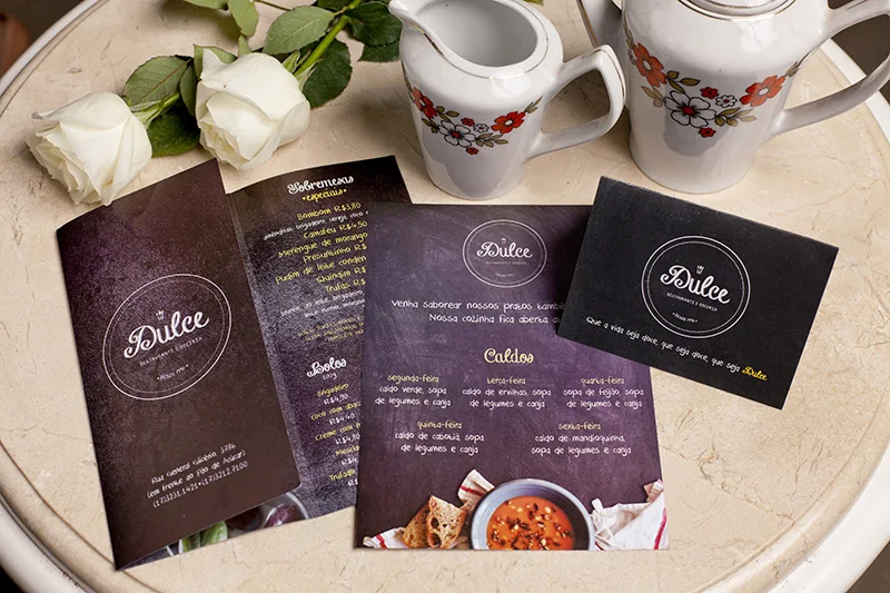 Cardápios Dulce em marrom escuro, sobre mesa posta com rosas brancas e xícaras