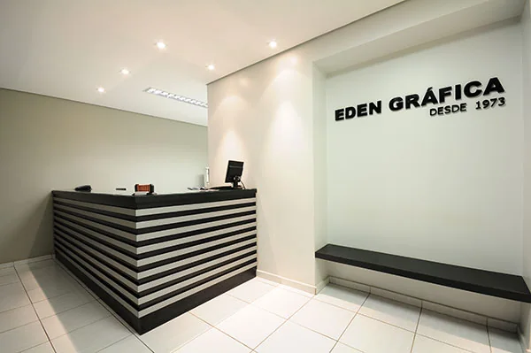 Recepção da Eden Gráfica: balcão listrado em preto e branco sob o letreiro "Eden Gráfica desde 1973"